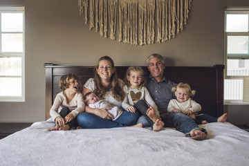 Portrait of happy parents with daughters sitting on bed at home