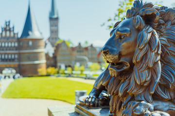 Bronze Lion statue in front of Holsten Gate - Holstentor, a city gate marking off the western boundary of the old center of Luebeck in Schleswig-Holstein, northern Germany