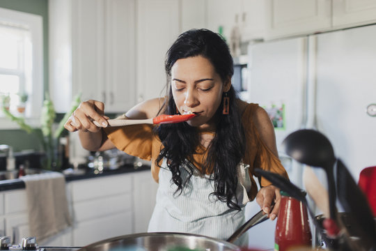 Woman Smelling Food On Spatula In Kitchen