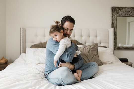 Portrait of sad daughter embraced by father on bed at home