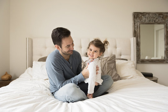 Smiling father with daughter siting on bed at home