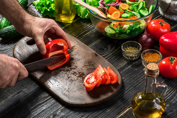 Man's hands cutting red paprika with knife. Cook cut red paprika. Man loves cooking fresh salad for dinner. Paprika cut by cook's hand.
