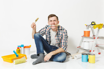 Fun mad crazy man sitting on floor with paint brush in mouth, instruments for renovation apartment room isolated on white background. Wallpaper gluing accessories, painting tools. Repair home concept.