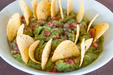 Guacamole dip from above with tomato pieces and tortilla chips on white bowl. Healthy snack food concept