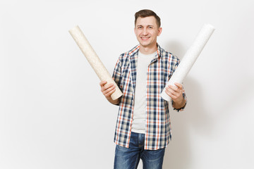 Young smiling handsome man in casual clothes holding wallpaper rolls isolated on white background. Instruments, accessories, tools for renovation apartment room. Repair home concept. Advertising area.