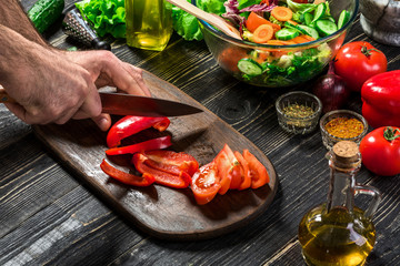 Man's hands cutting red paprika with knife. Cook cut red paprika. Man loves cooking fresh salad for dinner. Paprika cut by cook's hand.