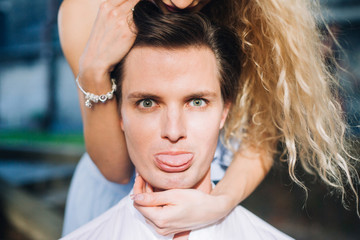 Emotional man's face closeup, newlyweds portrait, handsome man showing his tongue and making funny face while being hugged by wife