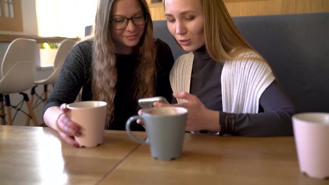 Two friends woman in cafe using mobile phone and have fun communicating