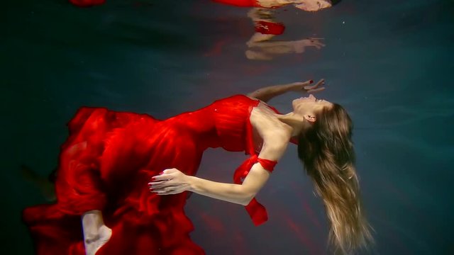 Attractive blonde woman floating underwater wearing beautiful red dress.