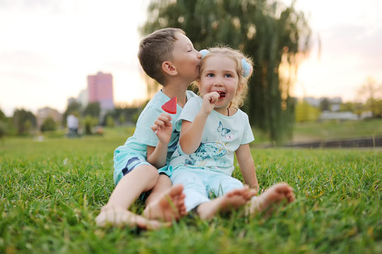 children - a boy and a girl are sitting barefoot on the grass and eating lollipops.