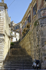 The classic moped at the base of the stairs leading through alley in Sicilian City of Modica, Italy