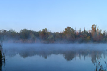 The dawn begins on the lake in the early morning, the reflection of trees from the opposite shore.