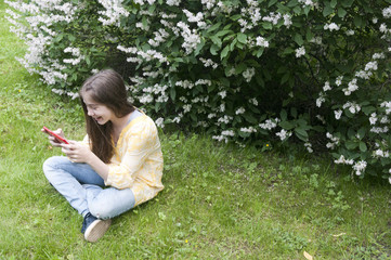 Beautiful teenager girl with tablet computer sits on the grass in Park. Photo