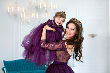 Happy princess girl with tiara dressed in purple dress, holds small daughter in her arms © popovatetiana