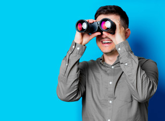 Young man looking for something with binoculars on blue background