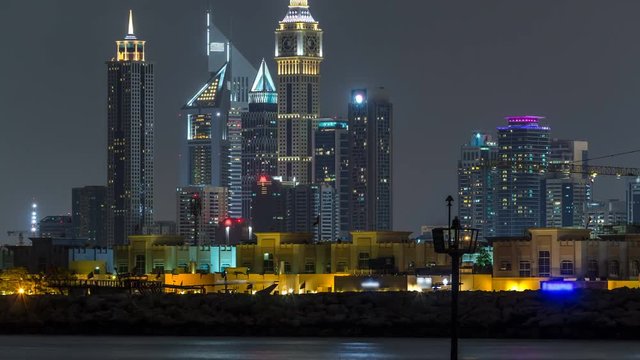 Modern Dubai city skyline timelapse at night with illuminated skyscrapers over water surface