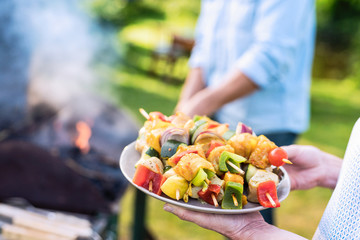 In summer. A couple prepares a bbq to welcome friends in the garden. Close-up on a plate of grill skewers