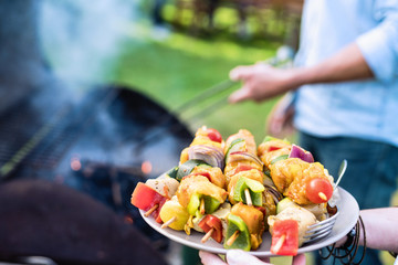 In summer. A couple prepares a bbq to welcome friends in the garden. Close-up on a plate of grill skewers