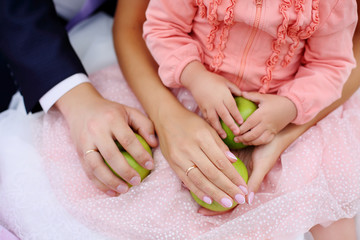 hands of the groom, bride with rings and their daughter with a green Apple