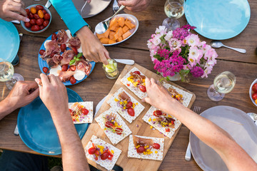 From above. a wooden table in the garden with food dishes and hands used for eating