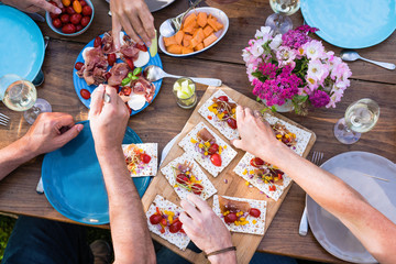 From above. a wooden table in the garden with food dishes and hands used for eating