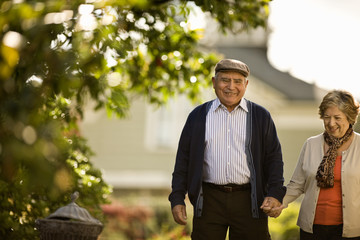 Mature couple hold hands as they walk together in a garden.