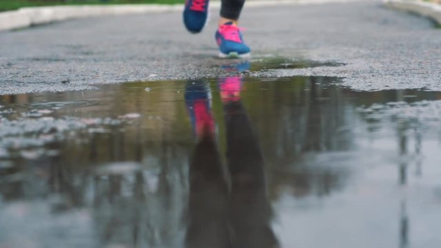 Close up slow motion shot of legs of a runner in sneakers. Female sports man jogging outdoors in a park, stepping into muddy puddle.