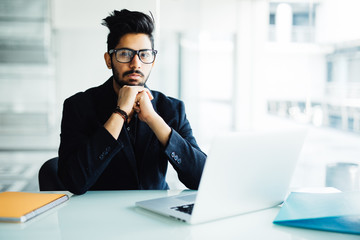 Fototapeta premium Indian business Man using laptop with hands hand on chin in his modern office