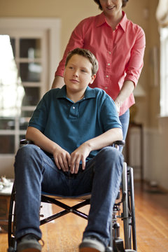 Teenage boy sitting in a wheelchair while his mother stands behind him.