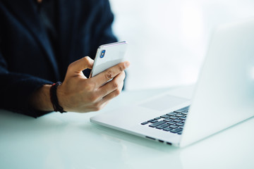close up of businessman using mobile phone and laptop computer on desk in modern office