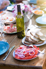 Close-up on a plate with tomato and onion slices on a table in a garden where friends gather to share a meal.