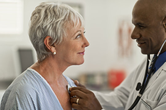 Mature Woman Gazes Flirtatiously At The Young Doctor Checking Her Heartbeat.