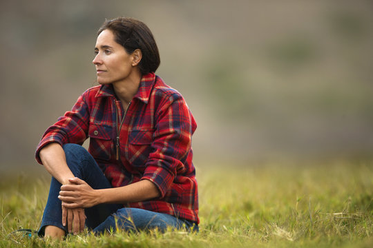 Portrait of a thoughtful mid adult woman sitting in a grassy field.