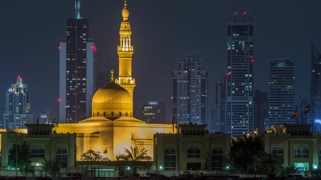 Modern Dubai city skyline timelapse with Rashid Al Hadeeth Mosque at night with illuminated skyscrapers over water surface