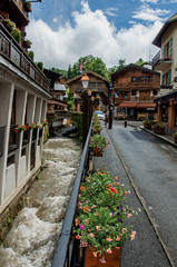 Typical buildings in street with cold water creek and alpine view in a cloudy day at Megeve. A famous ski resort located in the Haute-Savoie Province, near the Mont Blanc in the French Alps.