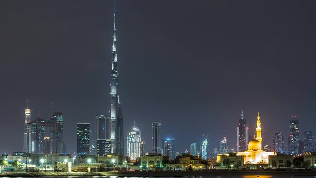 Modern Dubai city skyline timelapse at night with illuminated skyscrapers over water surface