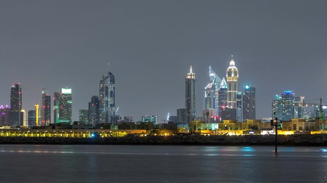 Modern Dubai city skyline timelapse at night with illuminated skyscrapers over water surface