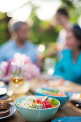 Close-up on a colorful salad in a bowl, Friends gather to share a meal around a table in the garden. Focus on the foreground