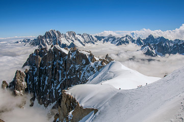 Snowy peaks and mountaineers in a sunny day, viewed from the Aiguille du Midi, near Chamonix. A famous ski resort located in Haute-Savoie Province, at the foot of Mont Blanc in the French Alps.