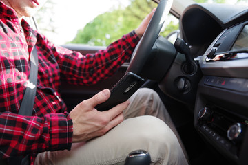 Mann schaut während der Fahrt auf sein Handy 