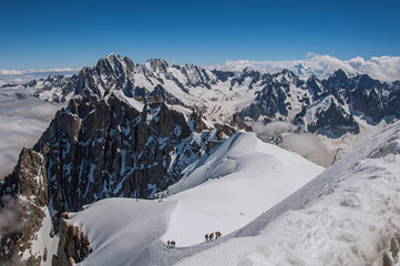 Snowy peaks and mountaineers in a sunny day, viewed from the Aiguille du Midi, near Chamonix. A famous ski resort located in Haute-Savoie Province, at the foot of Mont Blanc in the French Alps.
