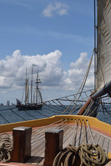 Historic tall ships sailing in bay, blue sky with clouds.