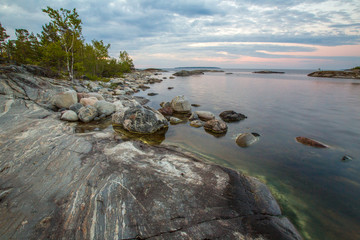 The gently sloping rock. White nights in Karelia. Rocky coast. The shore is strewn with stones. The natural landscape of Russia. Nature of Karelia. Ladoga lake.