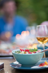 Close-up on a colorful salad in a bowl, Friends gather to share a meal around a table in the garden. Focus on the foreground