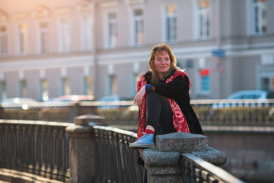 Pretty girl sits on the railing of the canal embankment in St. Petersburg.