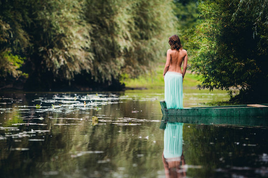 brunette in a turquoise skirt stands with a naked back in a boat on a river in the park in the summer