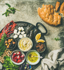 Mediterranean, Middle Eastern meze starters platter. Flat-lay of stuffed pickled paprikas, dolma, hummus, spiced oil, olives, sundried tomatoes, nuts, cheese, flatbread on tray, copy space top view