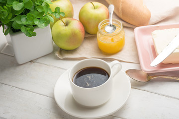 Morning cup of coffee, alarm clock, apples, butter and baguette, in a light kitchen. Background area, the concept of a bright morning and breakfast.