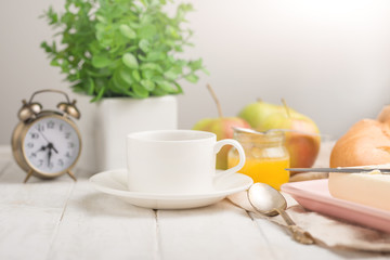 Morning cup of coffee, alarm clock, apples, butter and baguette, in a light kitchen. Background area, the concept of a bright morning and breakfast