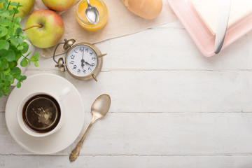 Morning cup of coffee, alarm clock, apples, butter and baguette, in a light kitchen. Background area, the concept of a bright morning and breakfast. Top view, with empty space for inscription